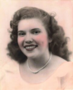Close-up portrait of a smiling woman with curled hair wearing a pearl necklace.