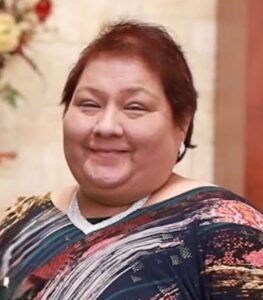 Smiling woman with short dark hair wearing a multicolored patterned top, posing for a portrait in an indoor setting.