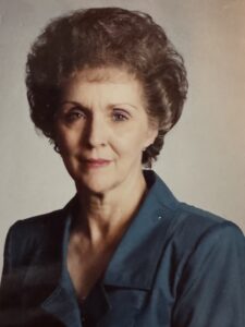 Head-and-shoulders portrait of a mature woman with short, dark hair wearing a teal blazer, looking at the camera with a subtle smile.