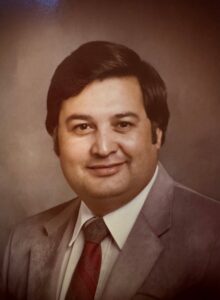 Smiling man in a brown suit and red tie, photographed as a cropped head-and-shoulders portrait (vintage photo).